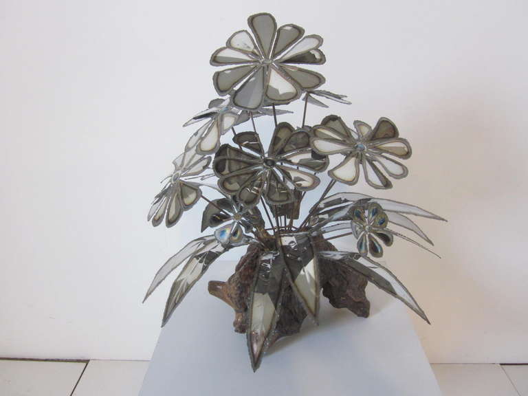 A welded, flamed and torch cut flower sculpture mounted on a natural formed wood base. The metal has been toned with heat to bring out depth and shadows to the piece.
