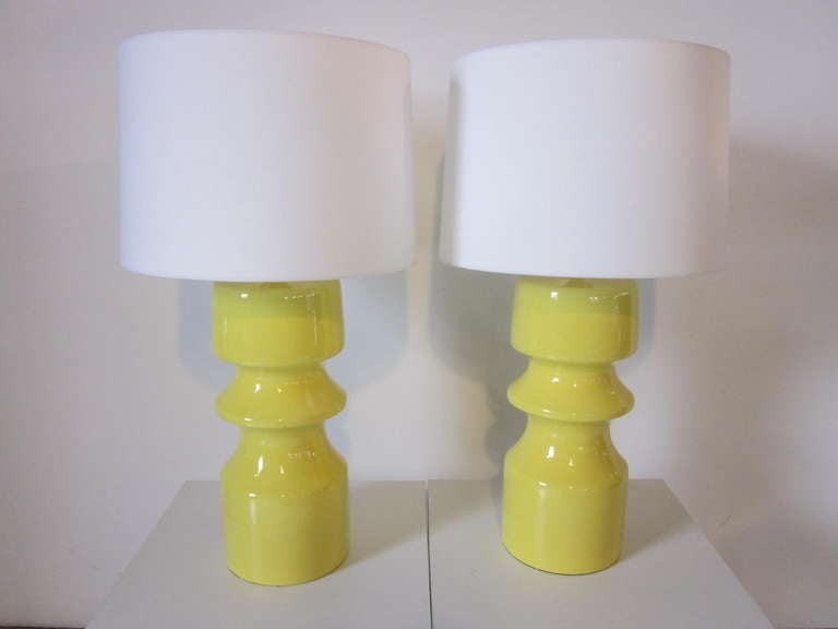 A matching pair of lemon yellow ceramic table lamps with sculptural bases and white linen shades.