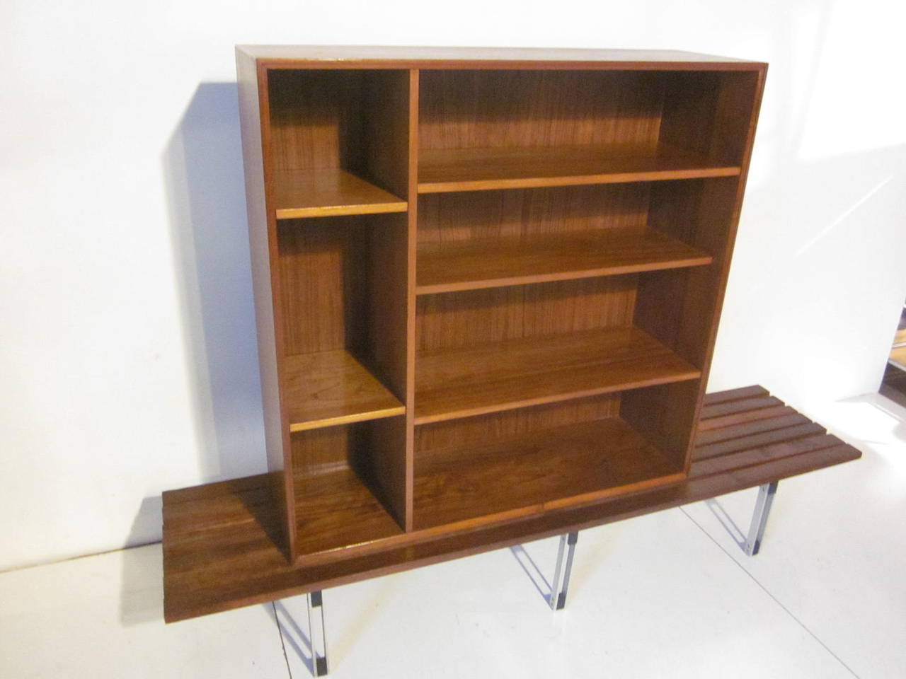 A teak wood bookcase that has adjustable shelves sitting on a slat wood bench with architectural styled metal leg supports. This two piece unit is excellent for a very light and streamline look. The bookcase itself, dimensions are 12.50
