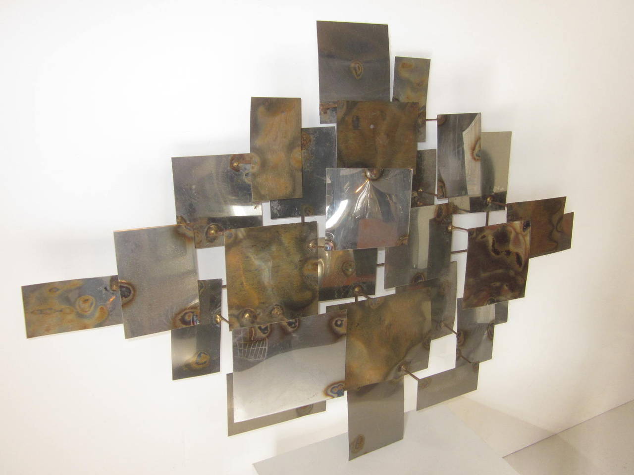 A patchwork metal wall sculpture with touched, burnt and welding chrome, copper and brass toned panels in the manner of Curtis Jere.