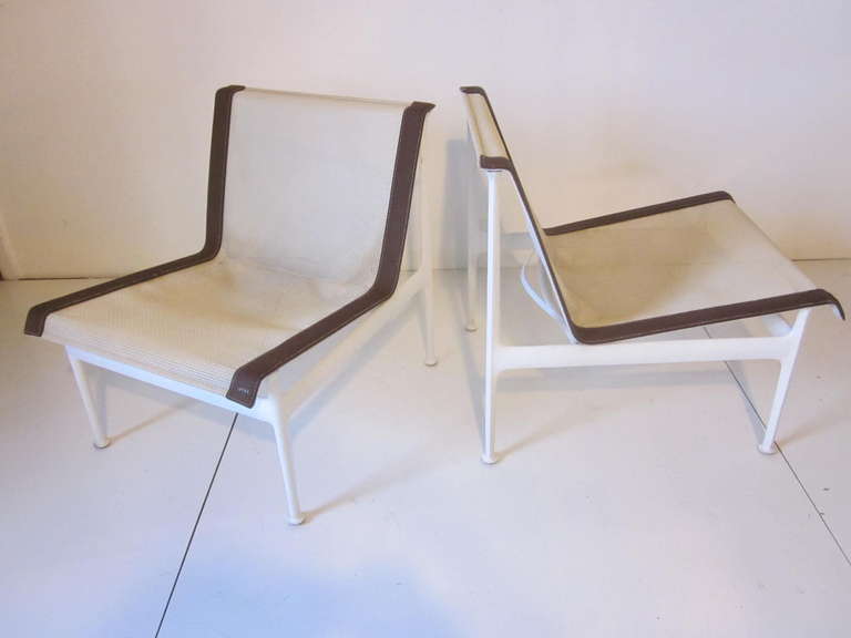 A pair of lounge chairs with off white mesh seating, brown leather type edge trim sitting on white powder coated aluminum bases. From the 1966 Collection from Knoll International.