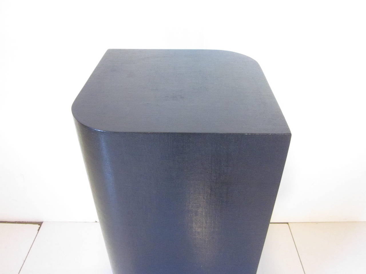 A linen covered rounded and pointed pedestal in black with lower brass wrapped banded detail in the manner of Karl Springer.