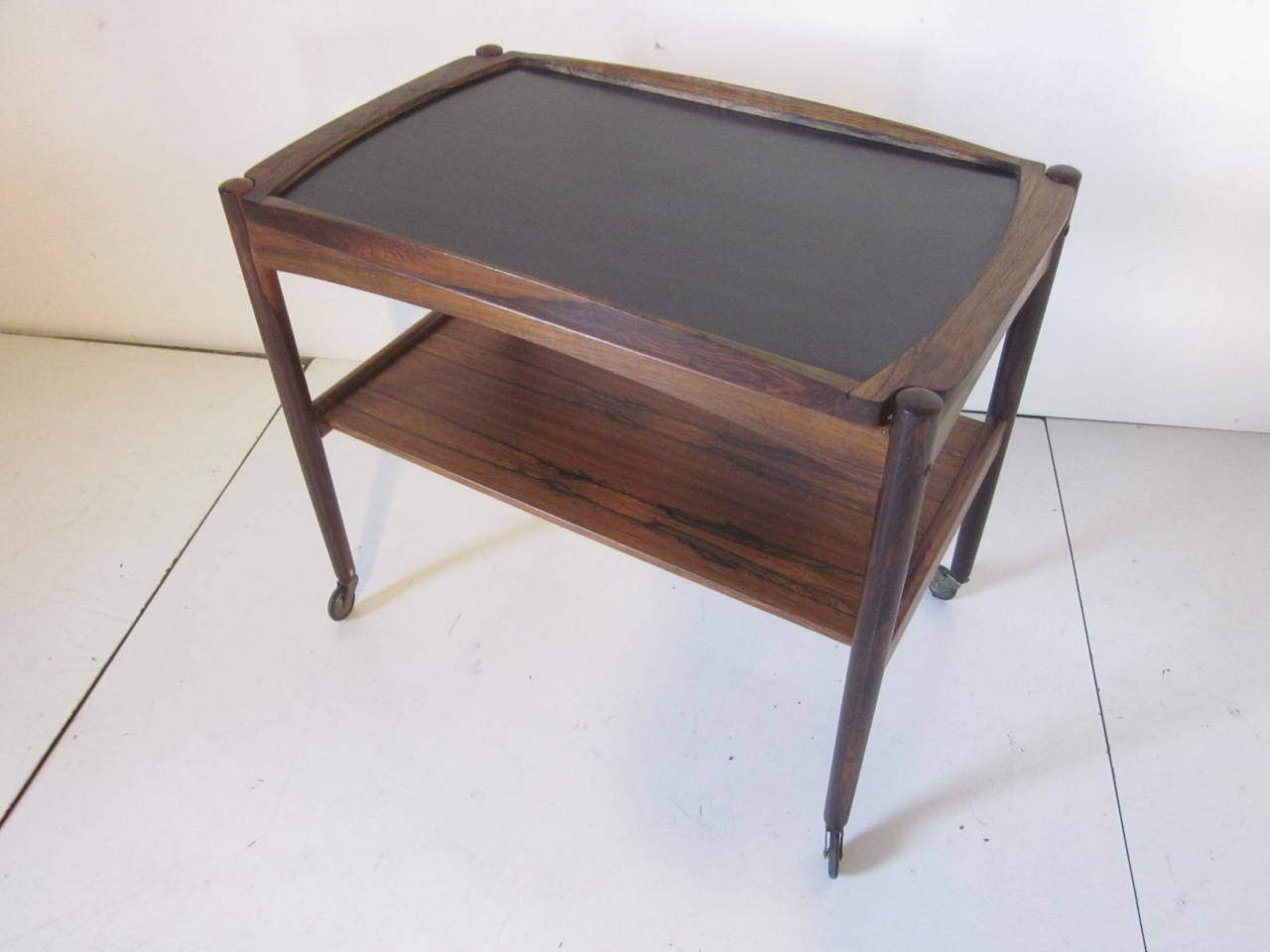A dark and rich Brazilian rosewood bar or serving cart in the manner of Arne Vodder with removable top which has a black laminate insert, lower shelve and metal wheels with rubber tread. Made in Denmark.