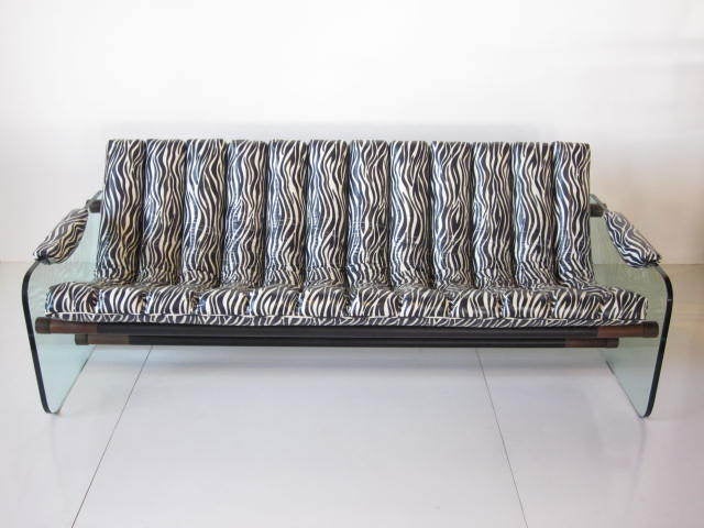 A glass sided sofa with zebra printed high quality vinyl coated fabric cushions and armrests supported by three black metal and walnut lower cross brace poles.In excellent vintage condition.Mfg.Craft Associates Inc.