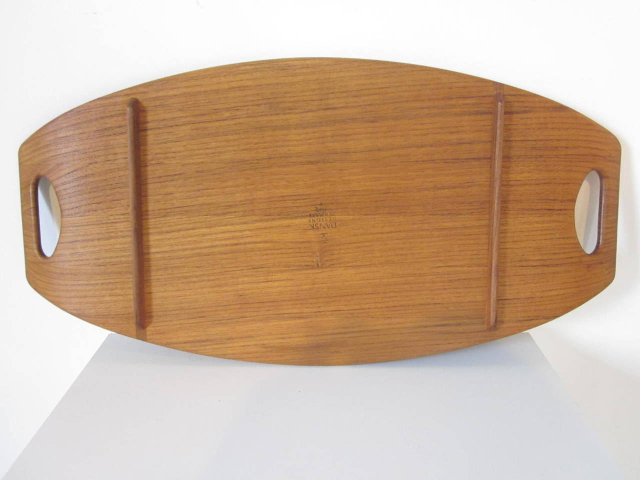 A large teakwood serving tray with side rail and leg rail design, two cut-out handles one of Quistgaard's most noted designs for Dansk. Branded mark to the bottom made in Denmark by Dansk.