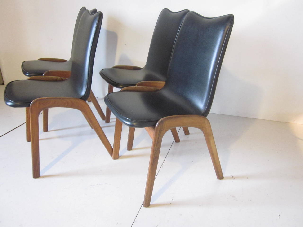A set of four sculptural solid walnut legged dining chairs with leatherette black upholstery in the manner of designer Adrian Pearsall. A light look but sturdy and well made.