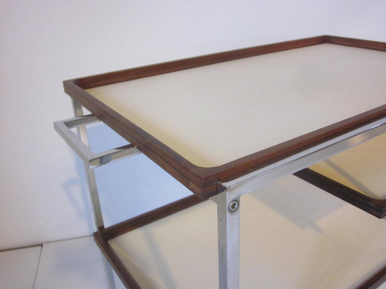 A Danish three removable tray bar or serving cart with chrome squared cart and wheels, each tray is framed in Brazilian rosewood with off white laminate inserts. Retains the manufactures and Danish control tags, Georg Petersens, Selectform
