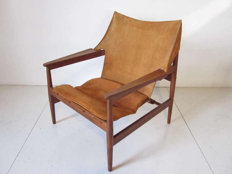 A dark teak wood and suede leather sling styled lounge chair with lower bucket strap supports ,matching loose bottom cushion and sculptural arms. Made In Denmark.