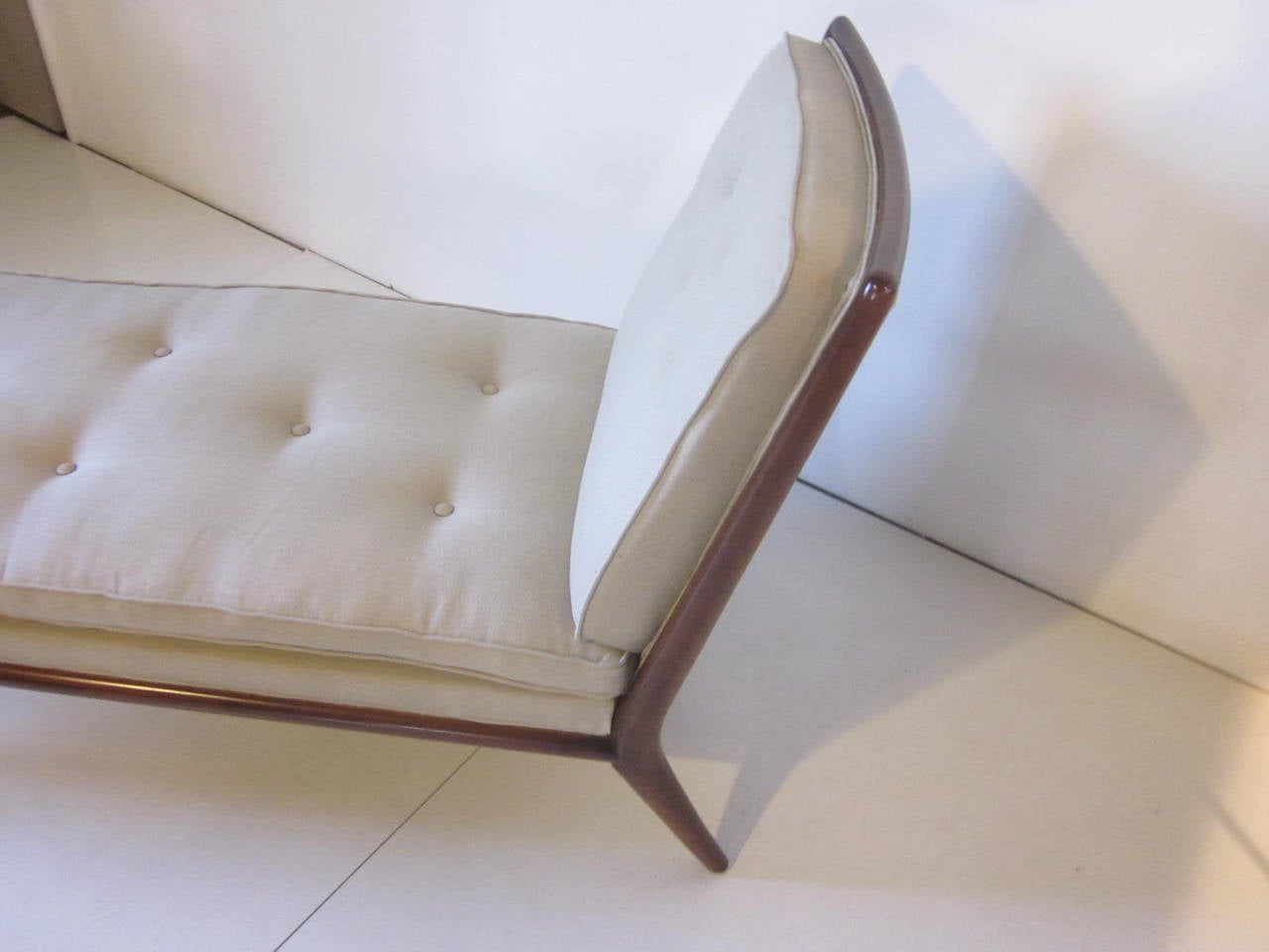 A chaise lounge chair by T.H. Robsjohn-Gibbings with dark mahogany frame, conical legs and buttons to the back and bottom cushions upholstered in Italian linen, a statement piece for any room, manufactured by the Widdicomb Furniture Company, Grand