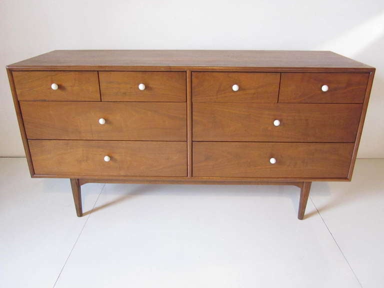 A medium colored flamed walnut dresser/ chest with four smaller top drawers and four larger lower drawers.All complimented with the original round white porcelain pulls.Mfg.Drexel for their Declaration line. 
