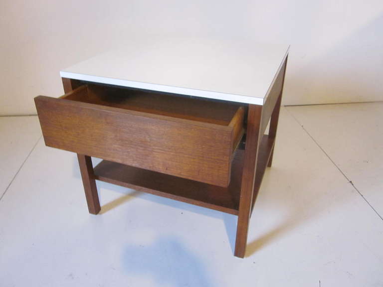 A single dark walnut nightstand or side table with upper drawer and lower shelve topped with a white laminate and retaining the early fabric Knoll tag to the inside drawer.