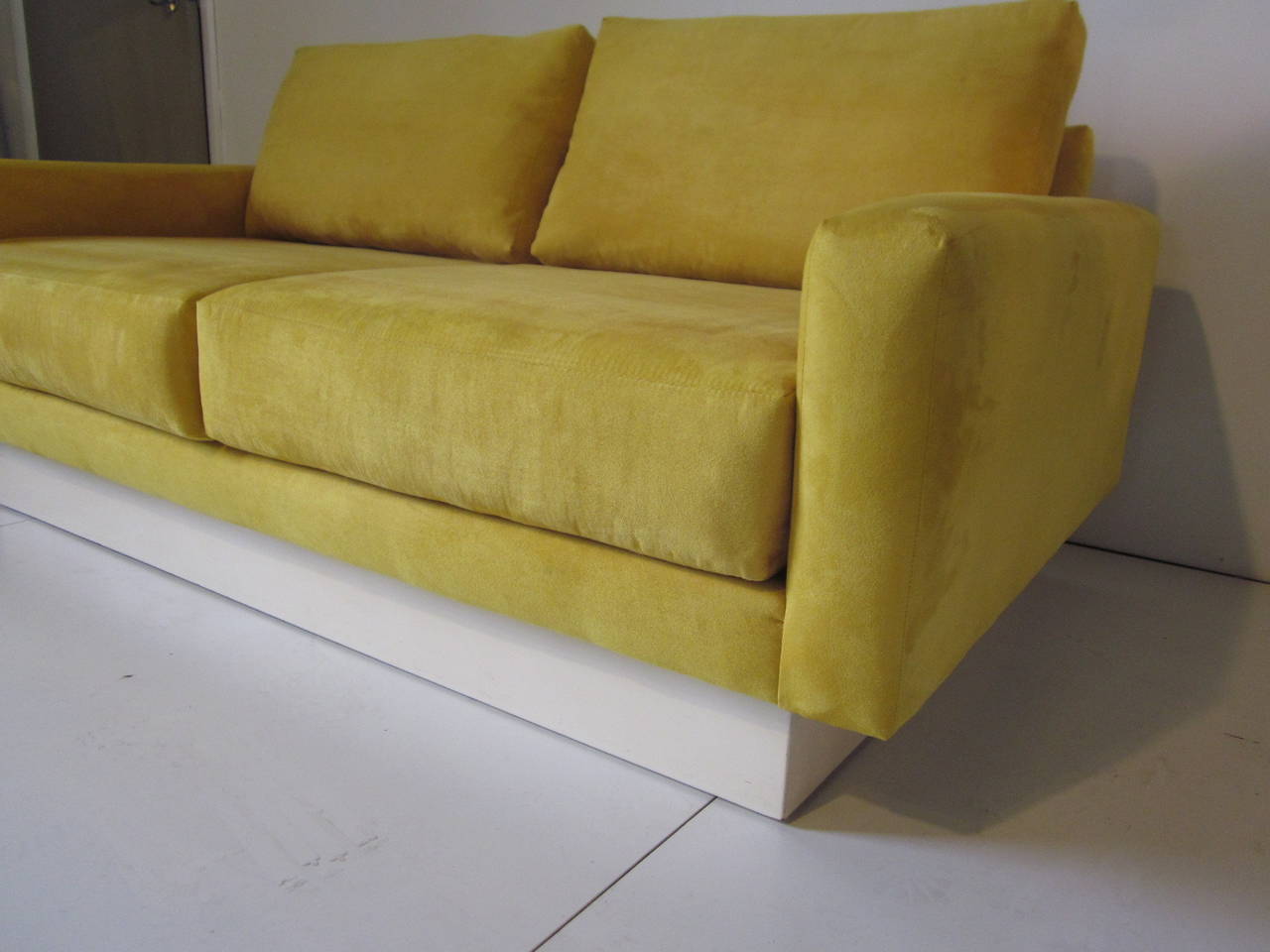 A Baughman loveseat with micro suede upholstery in a butter yellow, two back and two lower cushions sitting on a white base, manufactured by Thayer Coggin.