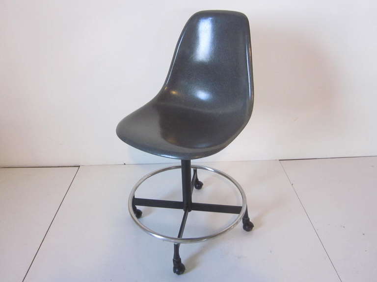 A dark gray fiberglass Eames adjustable, rolling swivel stool with chrome foot ring , the adjustment is made by turning the collar under the seat which goes from a seat height of 20
