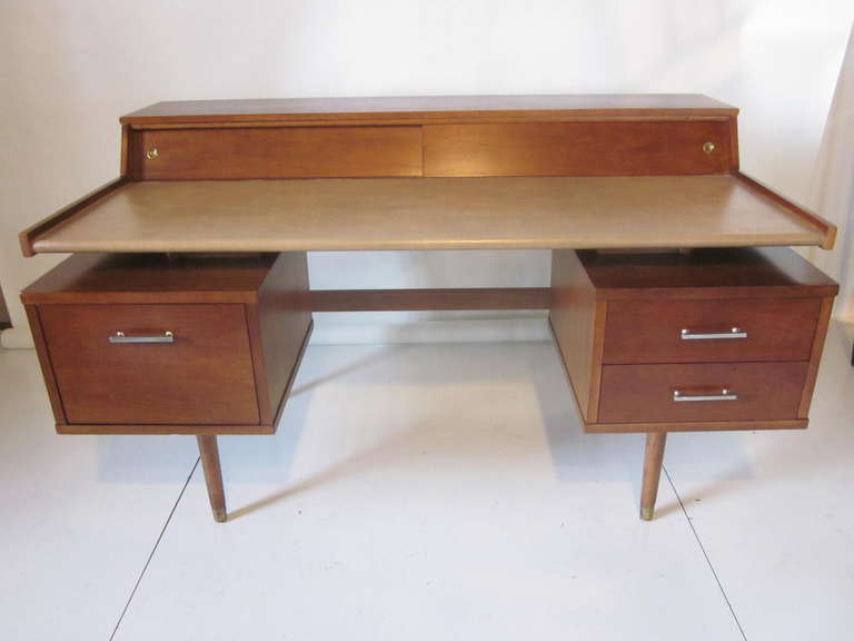 A true Mid Century classic desk from Drexel with upper storage compartment hidden by sliding wood doors, floating desk top covered in leather styled material. Two banks of drawers balance out the look with a file drawer to one side and pencil and