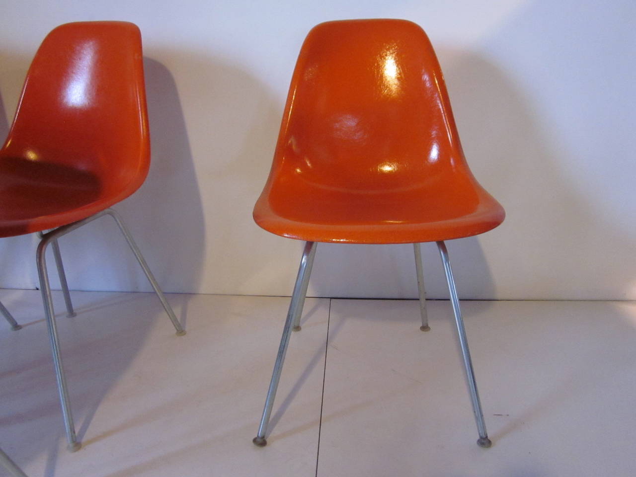 A set of six matching Eames bright orange fiberglass scoop chair sitting on zinc H-bases with white nylon feet. Retains some of the paper labels and impressed manufactures mark Herman Miller Furniture Company molded to the bottom.