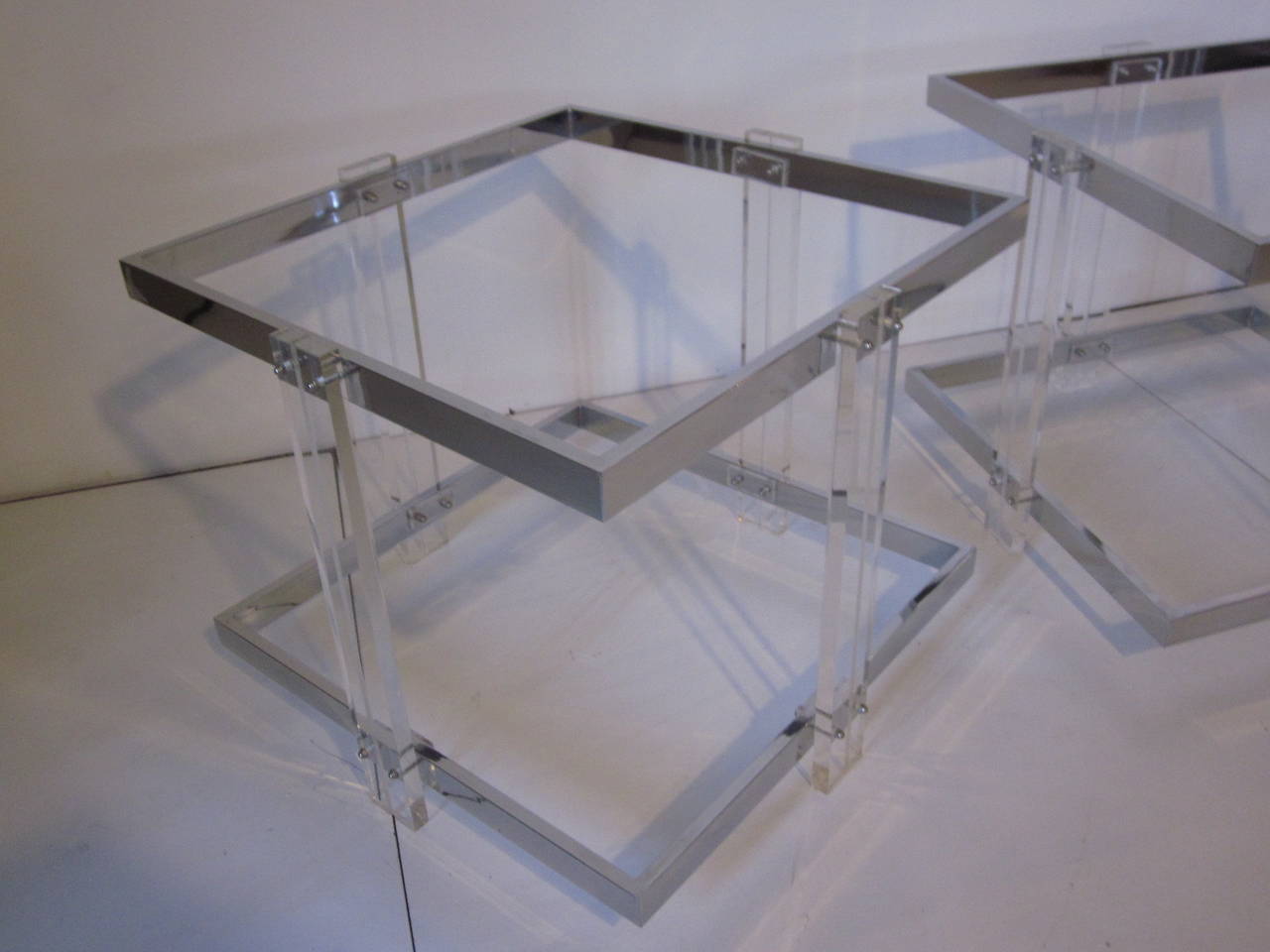 A pair of chrome and Lucite end tables with two plate glass shelves, Lucite legs with grooved detail and banded construction.