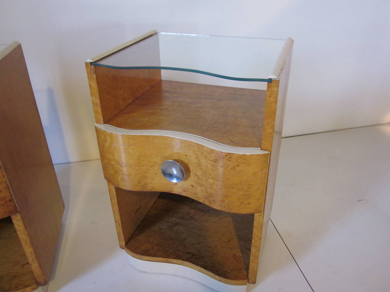 A pair of bird's-eye maple nightstands with drawer and large chrome pulls, upper and lower storage areas with matching contorted glass slide out top. Painted edge detail gives the nightstands a real dimensional look.