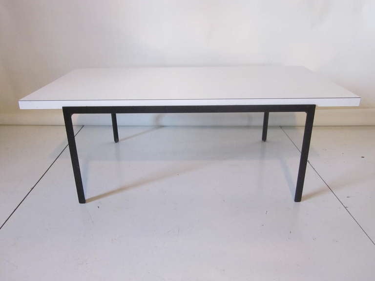 An earlier Knoll T - Angle coffee table with black iron T angle base which gives it the namesake with a white Formica top . Retaining it's original manufacturers label Knoll International.