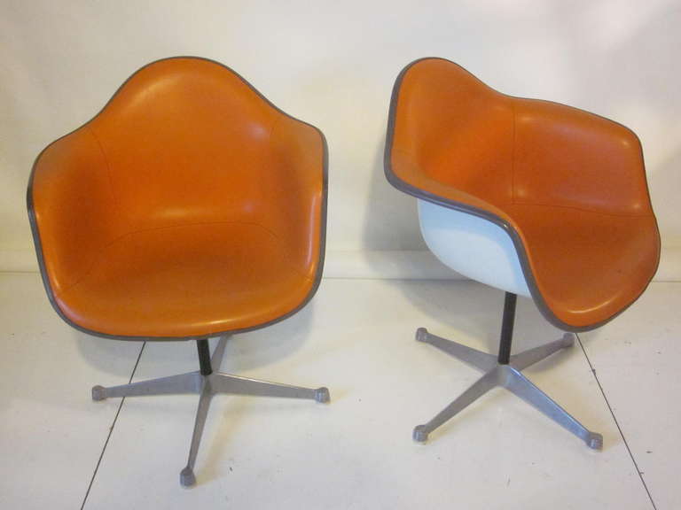 A pair of Eames swiveling arm shell chairs,white backs and upholstered in a pumpkin colored naugahyde sitting on aluminum star bases with nylon foot pads. Manufactured by the Herman Miller company from their Aluminum Group series.