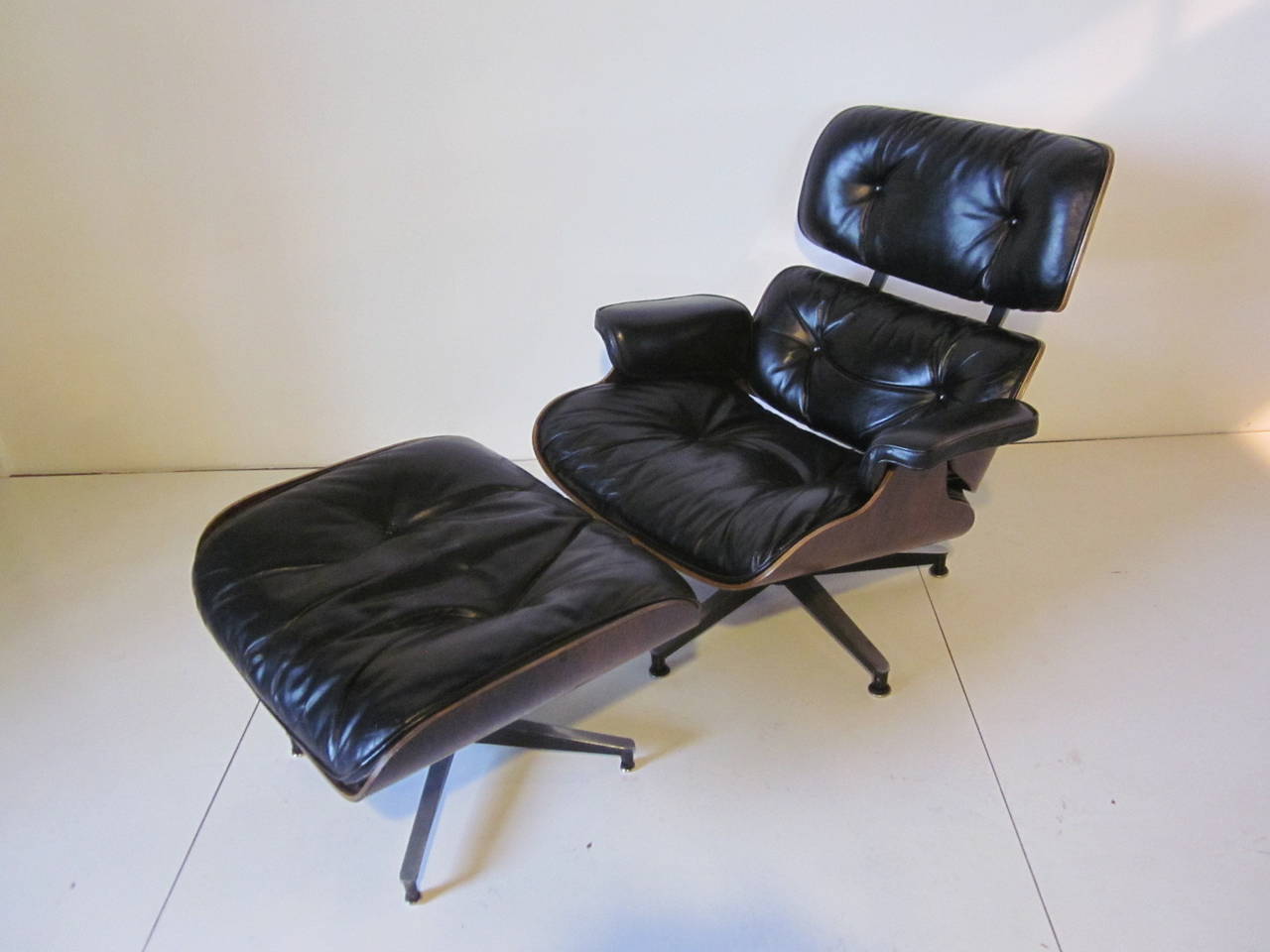 A rich and dark Brazilian rosewood Eames 670 lounge chair with ottoman, black soft leather seat cushions and cast aluminum swiveling bases, retains manufactures Herman Miller tags to the bottom as pictured. Ottoman size 26