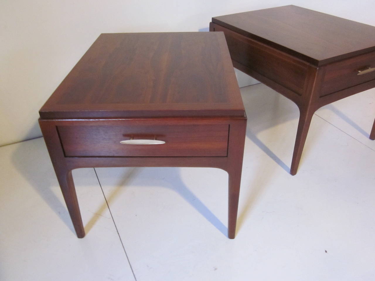 A pair of dark walnut nightstands or end tables with very well grained flamed walnut tops with a drawer to each complemented by brushed brass pulls.
