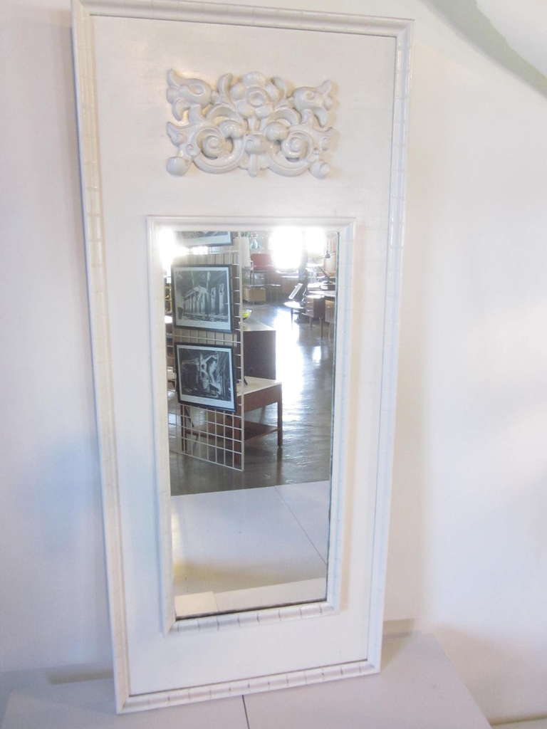 A white wooden mirror with carved wood design and notched details. Retains label to the verso manufactured by Complement .