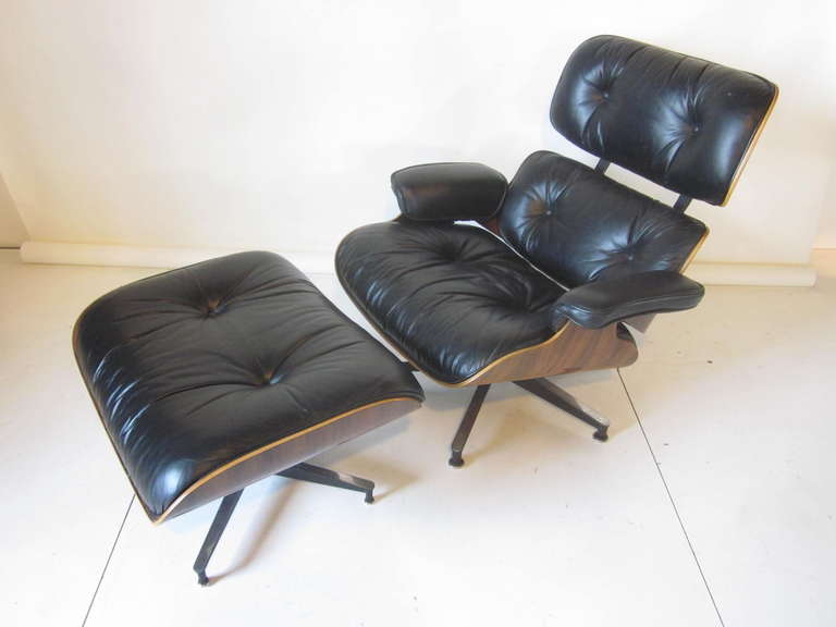 A dark and well grained Brazilian rosewood Eames 670 lounge chair and matching 671 ottoman in soft black leather. Sitting on cast aluminum bases with metal and rubber foot pads. A iconic design that's stood the test of time, retains labels and