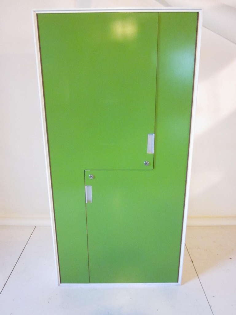 A bright green two door wardrobe with two pullout bins, aluminum handles and wood hanger bars. The doors are cut off set , an interesting design touch and facing small mirrors to each side. The back and sides are white with matching trim, a nice