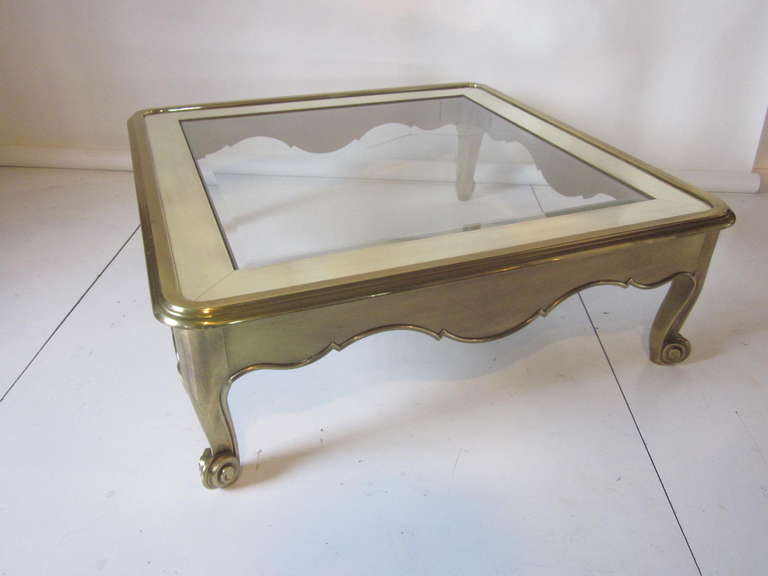 A scroll legged modern heavy brass coffee table with polished brass and glass top. Fine details in brass trim to the outer edge of the lower table bottom giving this piece a elegant baroque look. Manufactured and designed by Mastercraft Furniture