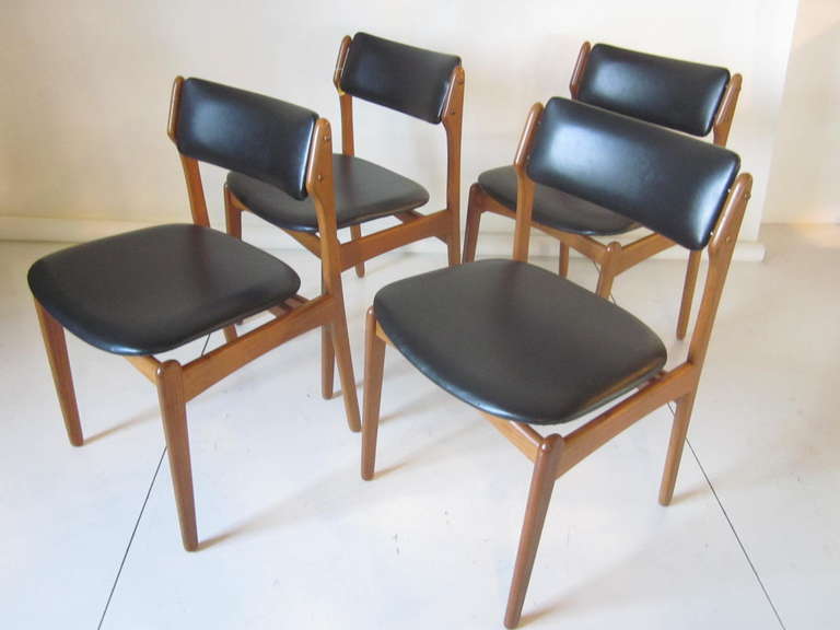 A set of teak wood Eric Buck dining chairs with black upholstered backs and seat bottoms and brass hardware detail to the upper seat back.