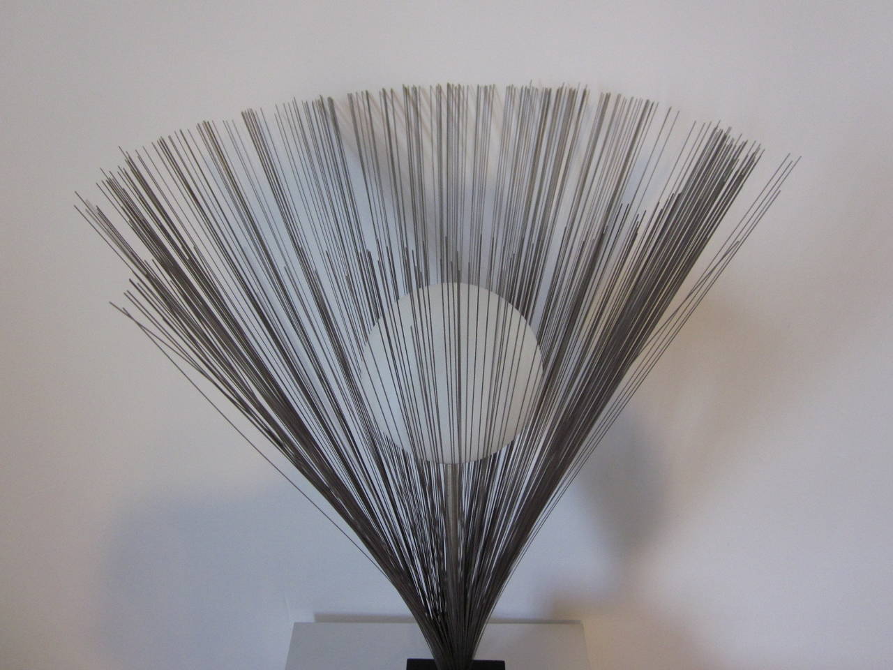 A metal wire spray sculptural table lamp in the manner of Harry Bertoia with chrome shafted and white frosted ball lamp shade mounted inside the spray on a black metal base which is 5.50