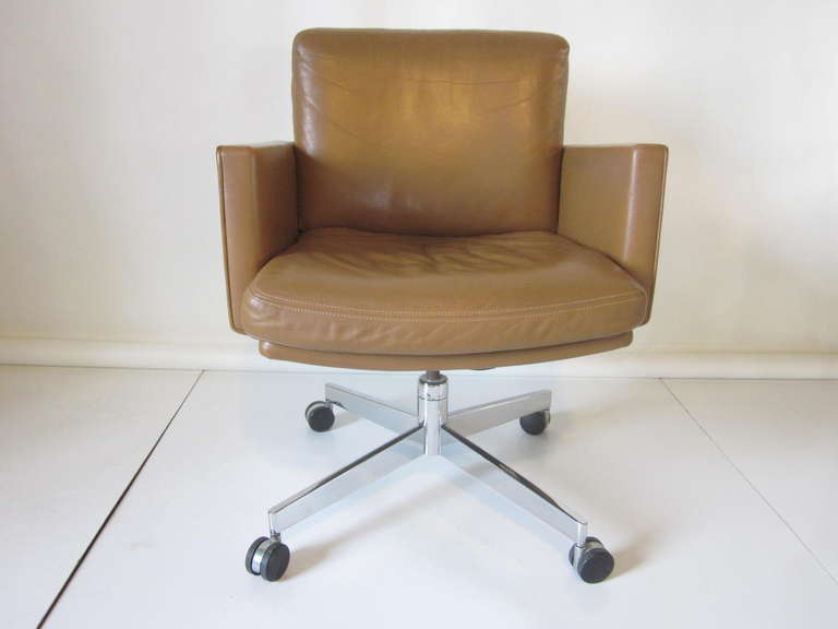 A executive desk chair with soft and high quality leather in a warm natural medium color sitting on a chrome swiveling adjustable rolling base. Retains the Manufactures label ,Stow Davis Furniture company.