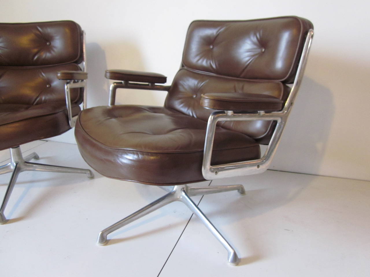 A pair of dark brown leather Time Life arm chairs with cast aluminum frame and swivel bases, nylon footpads are present to protect your floors and they both  retain the manufactures tag to the bottom from the Herman Miller Furniture Company.