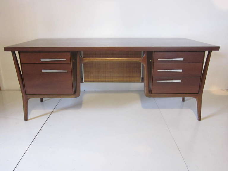 A fantastic Midcentury dark walnut desk with sculptural leg and frame design in the manner of Gio Ponti , a caned privacy panel to the front and drawers to each side with aero dynamic brushed stainless pulls. It has a large off set writing surface