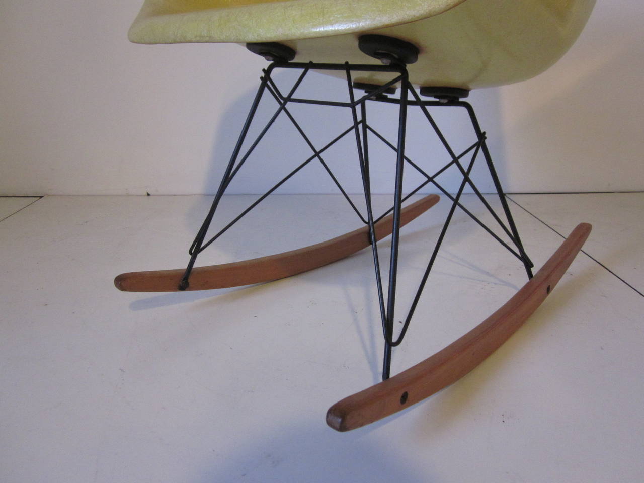 A very early Eames designed fiberglass arm shell rocking chair with rope edge, large shock mounts, satin black wire base and birchwood rockers. Retains the original decal to the reverse side designed by Charles Eames and manufactured by the Zenith