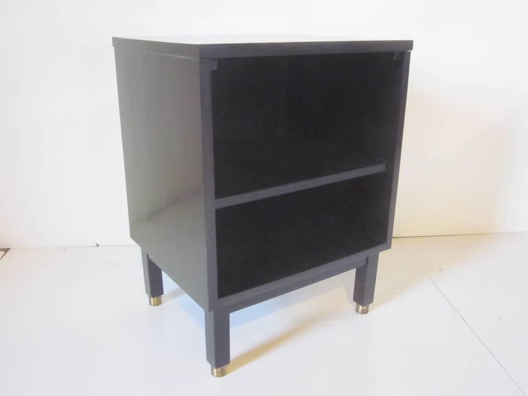 A dark ebony stained mahogany nightstand or side cabinet with brass capped legs and a top that is made of laminate but looks so close to wood that it's almost impossible to tell. Two open storage areas and it still retains the metal manufactures