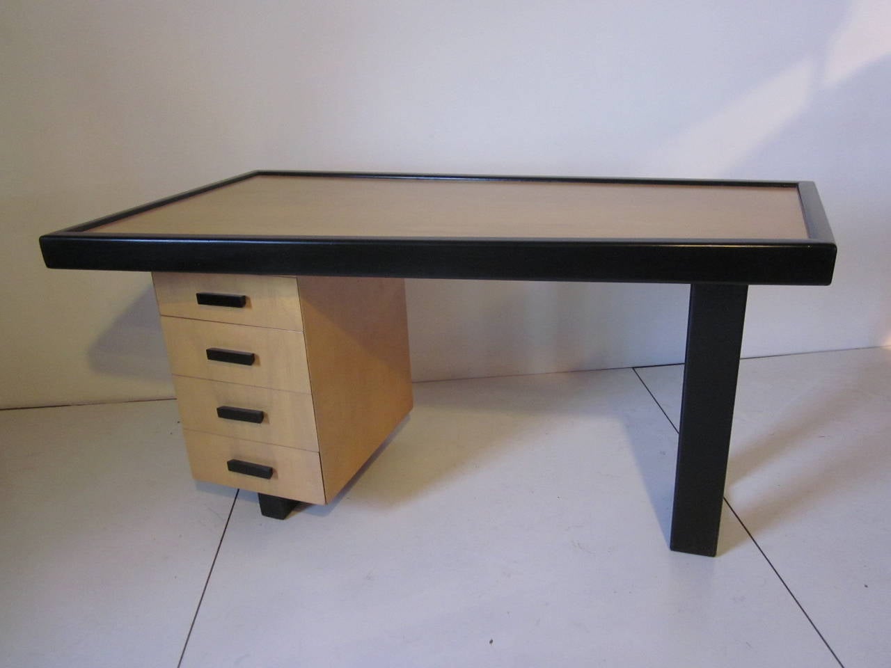 A trapezoid two toned black and clear wood desk with open ended leg and four drawers complemented by black details. Attributed to Eugene Schoen.