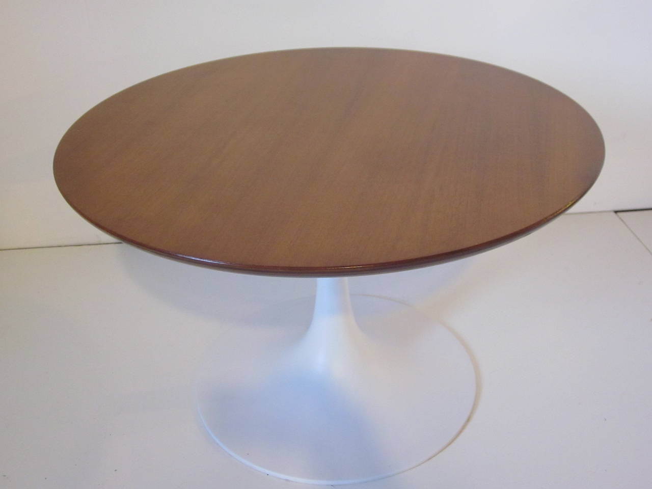 A tulip side table with satin white metal base and round walnut top in the style of Knoll International and Saarinen.