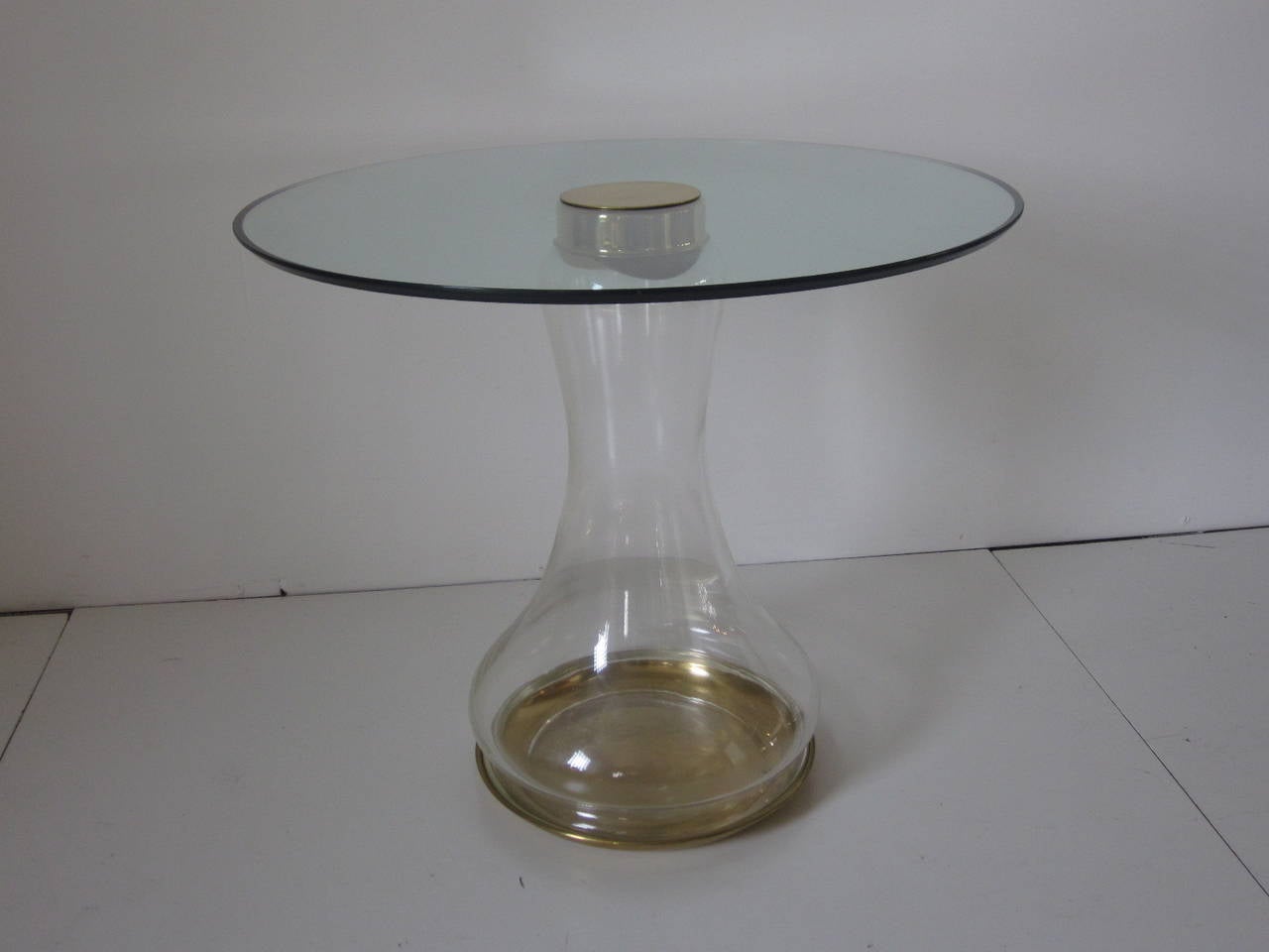 A handblown glass and brass based side table with screw on brass cap supporting a round beveled glass top. The base has a brass pan like tray for support which helps give the piece a rich and sculptural design aesthetic retaining labels made by