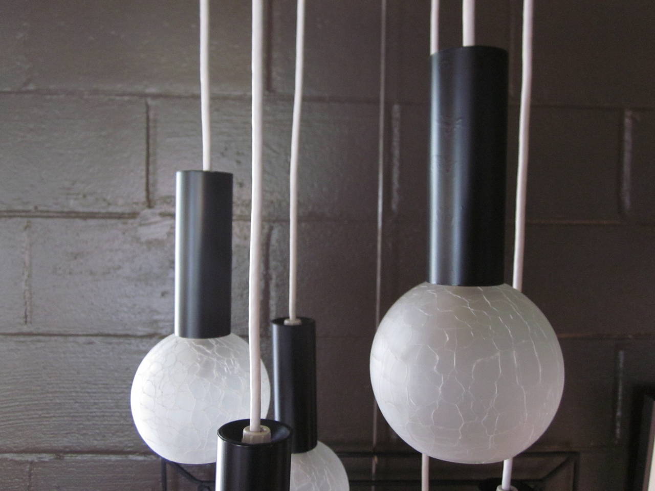 A Sciolari chandelier with six hanging lights, satin black steel shafts and round crackle glass balls, the mounting ceiling plate is a satin white metal with brass details. The length of each light can be slightly adjusted and modified with the cord