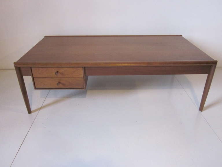 A medium colored two drawer Mid Century coffee table with tapered legs and matching wood pulls inset with metal detail.manufactured by the Drexel Furniture company from their Parallel Line.