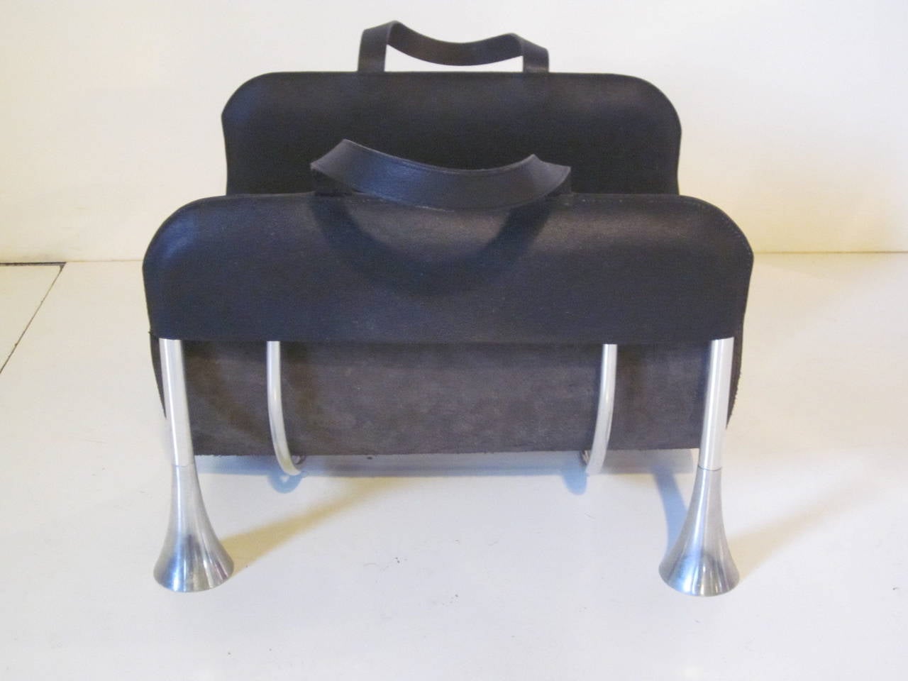 A black pebbled leather and aluminum log or magazine holder, used as a log holder it has a slip off leather carrier with handles for toting wood and could be used as a magazine rack and when done tote them to the recycling bin when finished.