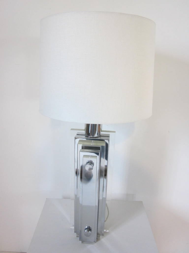 A Lucite and chrome layered table lamp with large chrome accent buttons and topped with a linen shade, retains the original Lucite final.