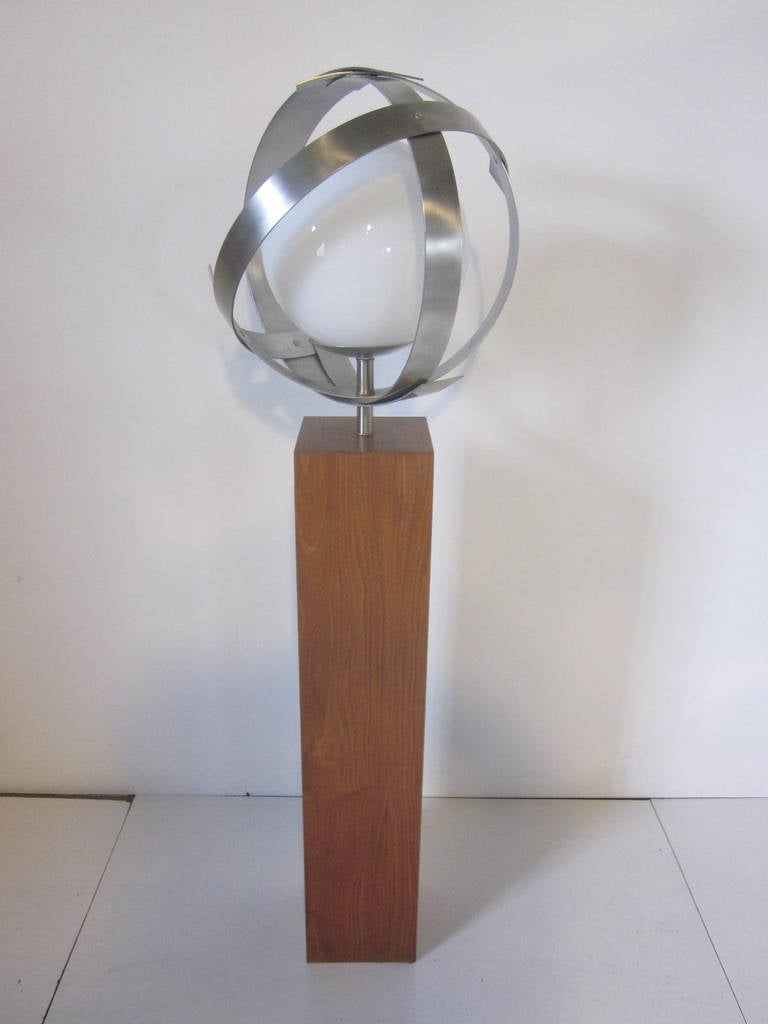 A sculptural aluminum banded floor lamp with large white opaque glass globe sitting on a walnut riser styled base, retains the original manufactures tag, made by the Laurel Lamp company.