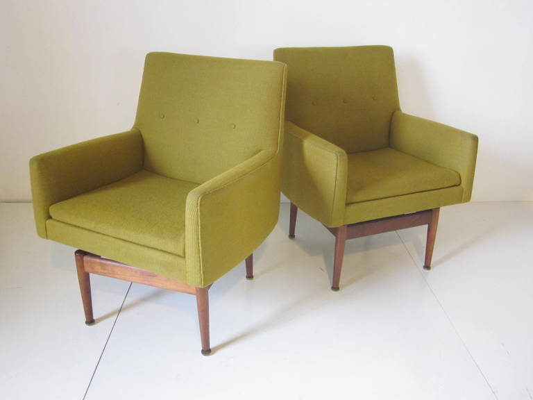 A pair of upholstered Risom swiveling lounge chairs with solid walnut bases, retains the original manufactures label Jens Risom Design Company, NY.