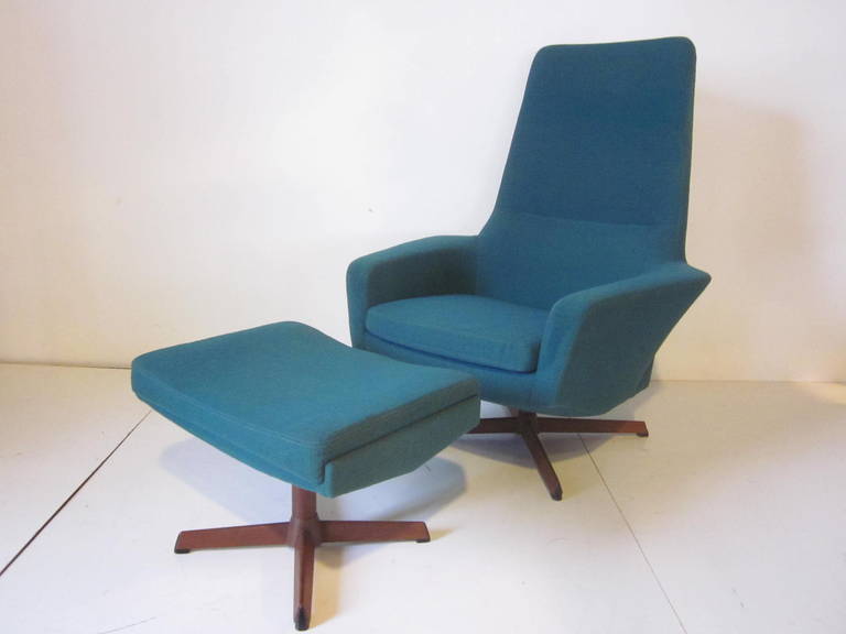 A Danish lounge chair and ottoman upholstered in a teal green / blue colored  fabric with teakwood star styled bases, the chair has swiveling and locking back and forth positions and retains the manufactures tag -Danish control ,Povl Dinesen Made in