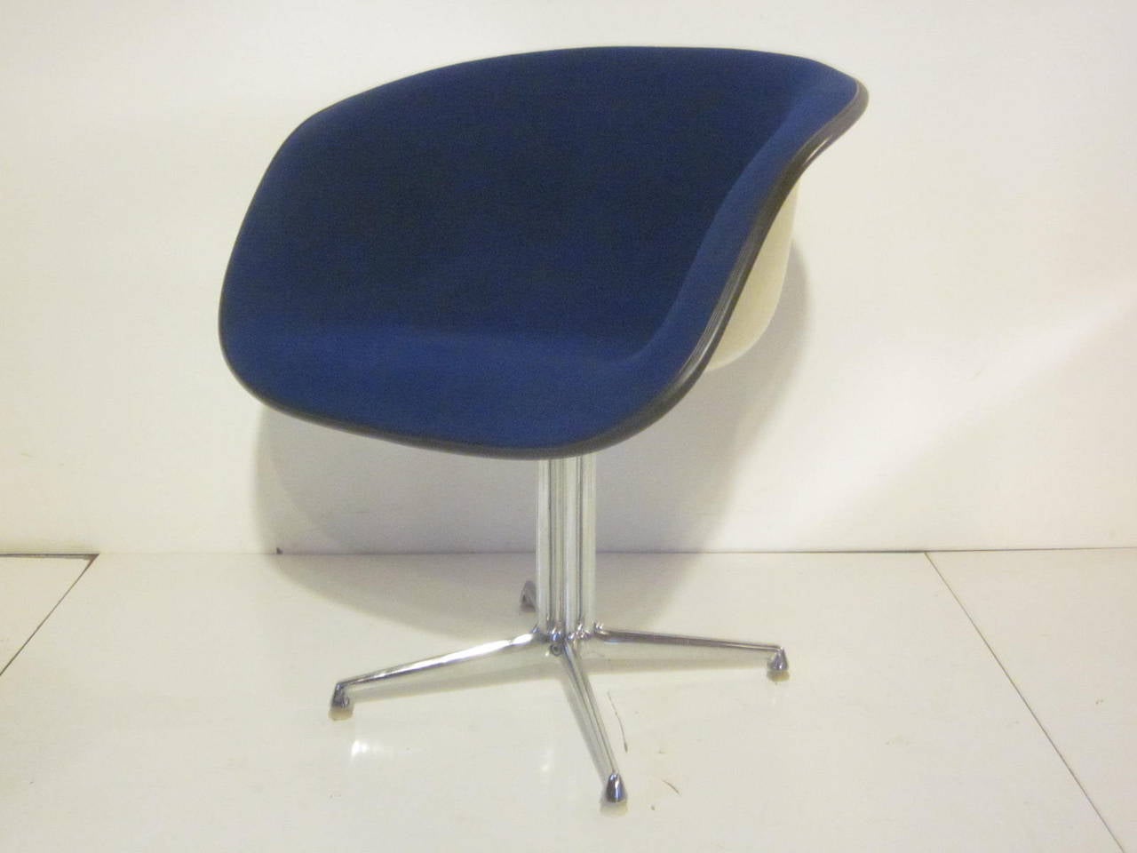 A blue upholstered Eames La Fonda chair with chromed base, off white fiberglass shell and bone toned plastic feet. Manufactured by the Herman Miller furniture company.