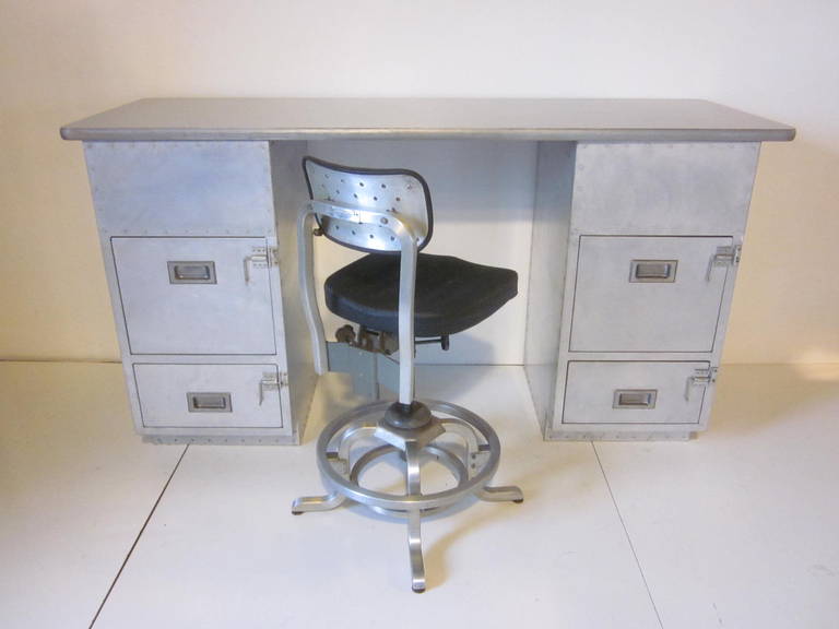 An Industrial styled desk or work bench with aircraft grade aluminum pedestals with drawers to each side and a wood top with simulated brushed aluminum surface and rubber edge. Included with the desk is a good form Industrial swiveling and