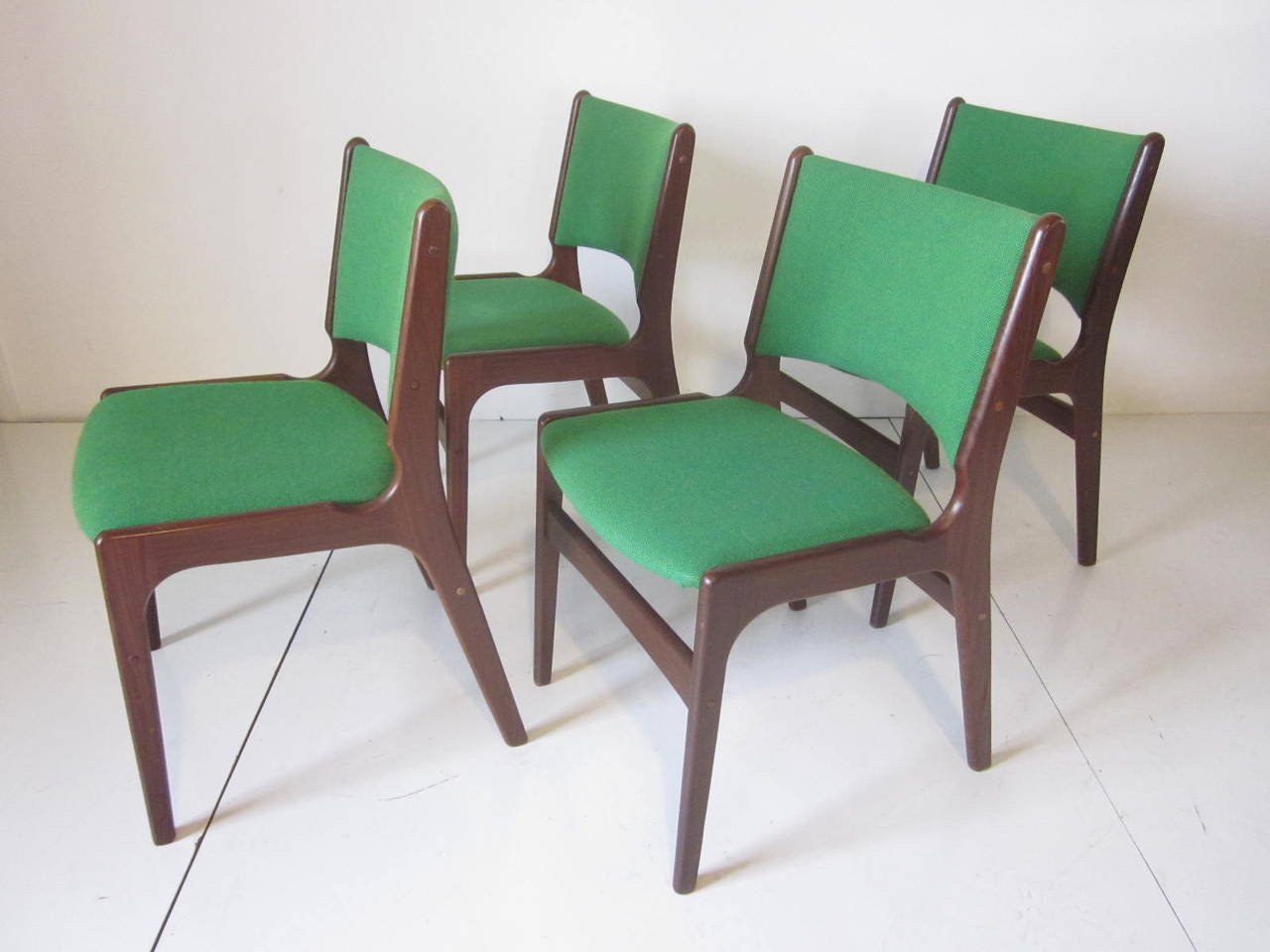 A set of four dark walnut framed dining chairs with bright green wool upholstery in the manner of Danish designer Eric Buck. Each chair is stamped to the bottom Made In Denmark.