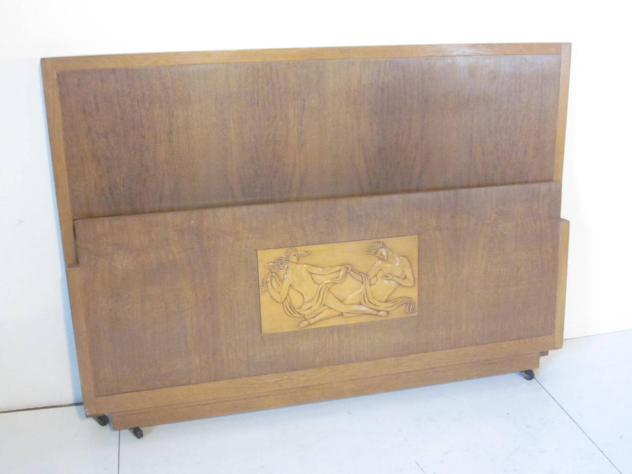 An Art Deco bed with relief to the foot board of a dream like man and woman motif set in well grained wood with matching headboard. This bed comes complete with matching wood side rails and bottom slats, will accommodate a standard full size